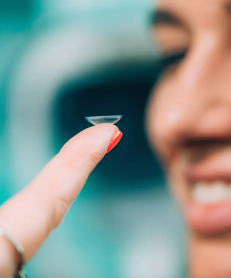 Clear contact lens balanced on a fingertip beside a smiling person